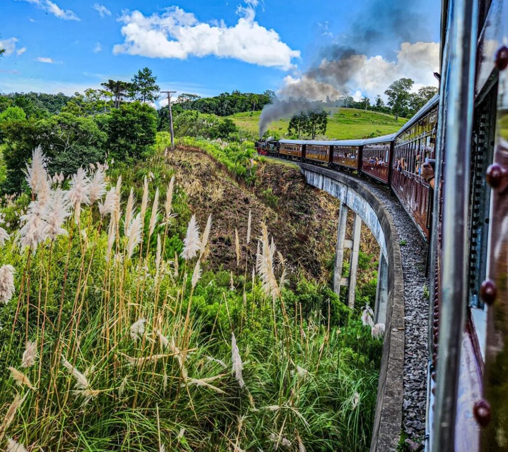 Foto do trem maria fumaça visto fazendo a curva, foto tirada da janela do trem
