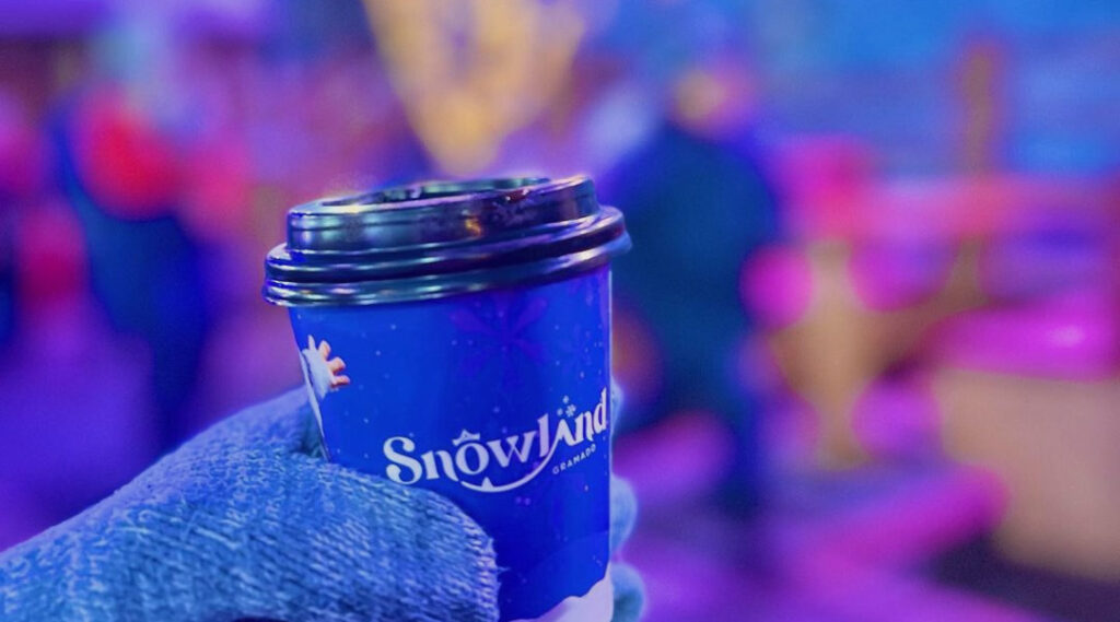 Pessoa com luvas nas mãos segurando copo de café com a logo do Snowland