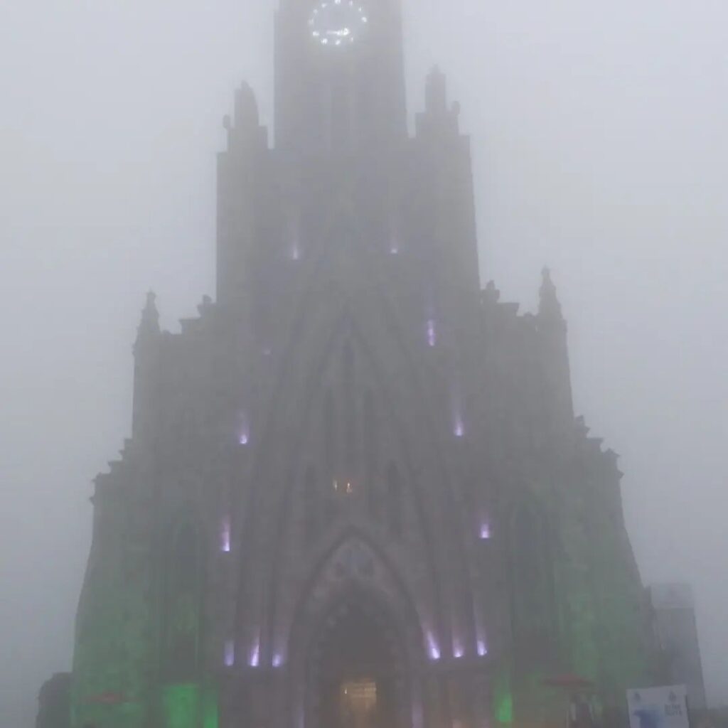 Foto da Paróquia de Nossa Senhora de Lourdes em Canela, a Catedral de Pedra está iluminada e envolta em neblina.