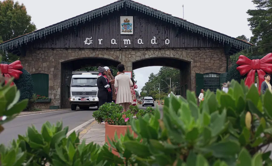 Pórtico de Gramado com pessoas tirando fotografias enquanto os carros passam