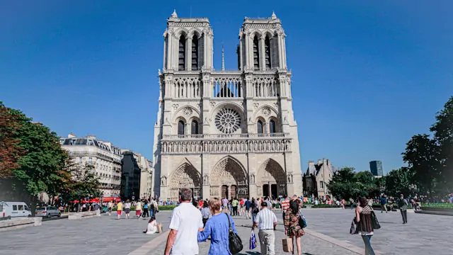 A foto mostra pessoas no pátio em frente a Notre Dame. Dia de sol. Ceu limpo e claro.